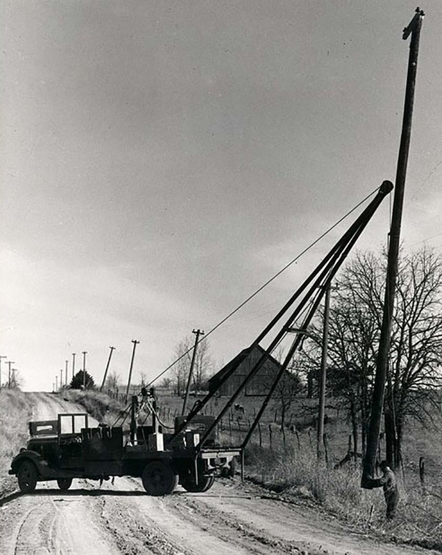 black and white photo of a truck setting an electric pole